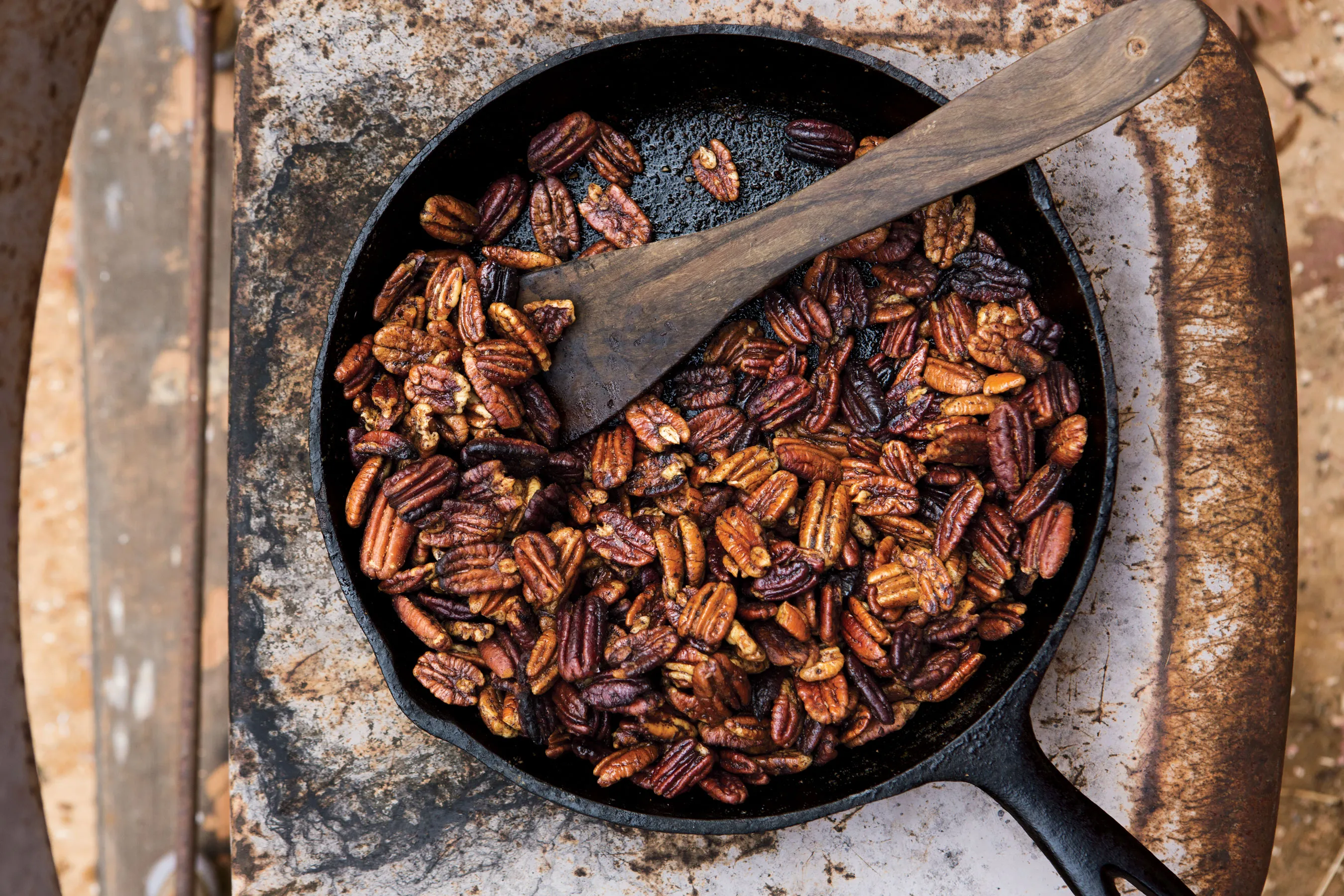 Pecan halves toasting in a dry skillet on a stovetop, with a wooden spoon stirring