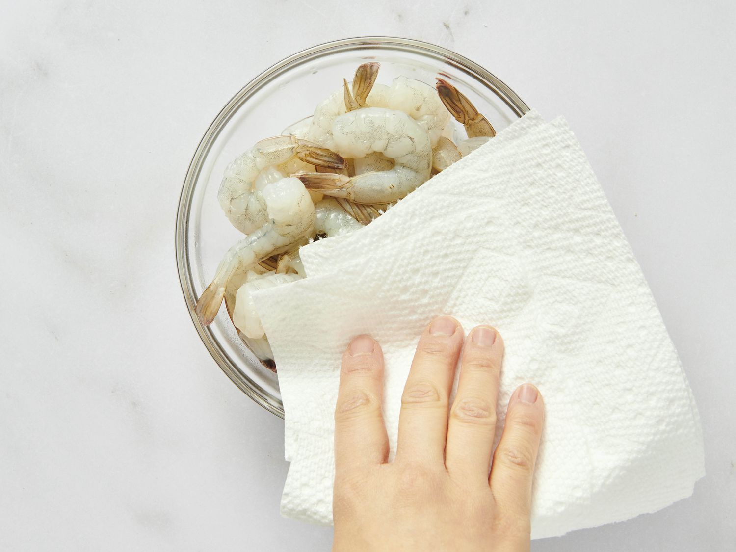 Peeled and deveined raw shrimp patted dry on paper towels on a kitchen counter next to a small bowl of salt and pepper