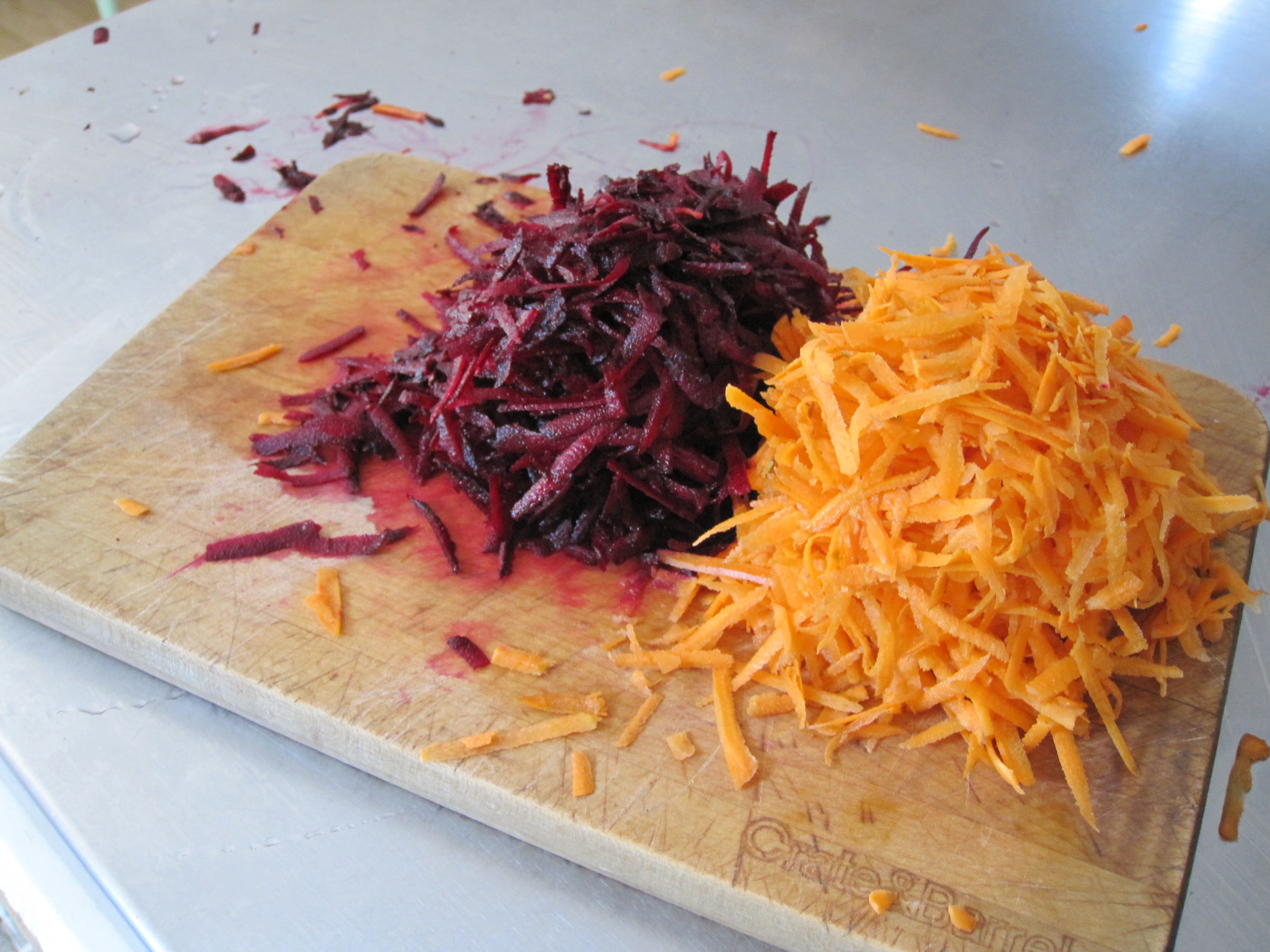 Peeled beets being grated on a box grater over a wooden cutting board with a bowl nearby