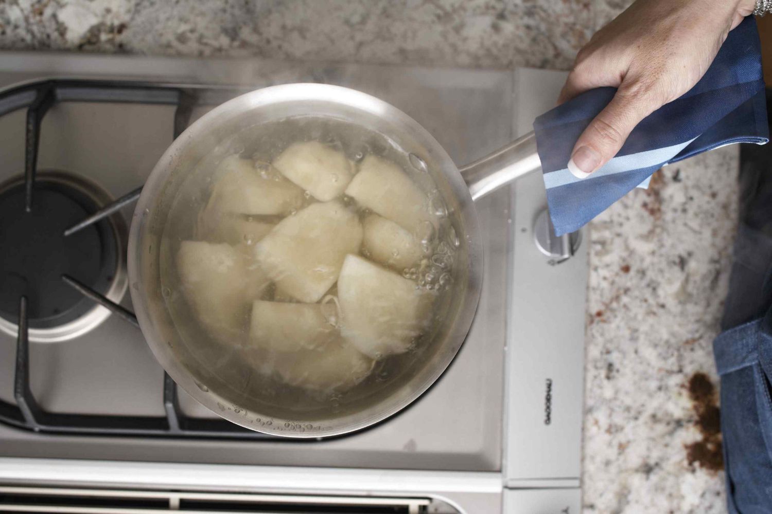 Peeled potato chunks simmering in a large pot of water on a stovetop with gentle bubbles