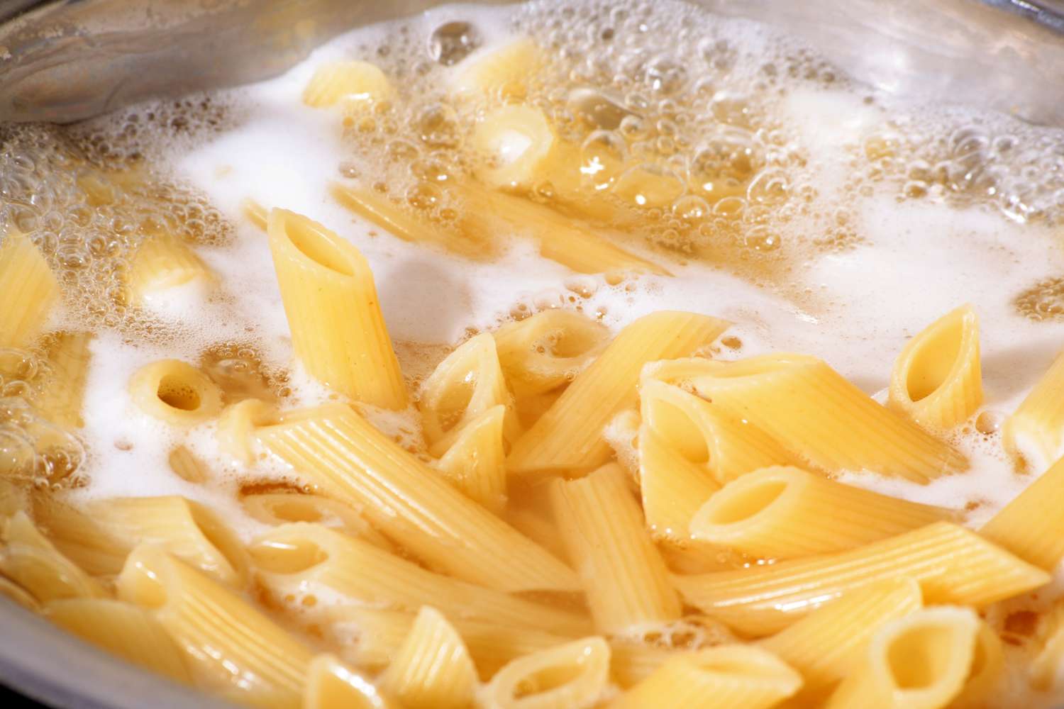 Penne pasta boiling in a large pot of salted water on a stovetop