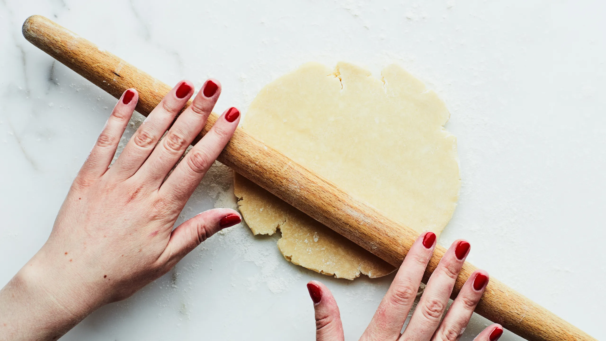 Pie dough being rolled with a rolling pin on a lightly floured kitchen counter