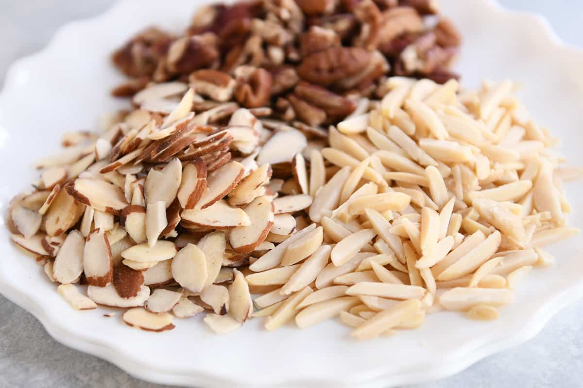 Pine nuts and slivered almonds toasting in a small skillet with melted butter on a home stove