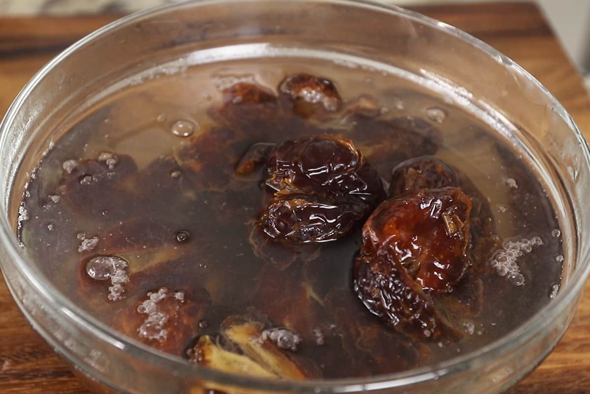 Pitted Medjool dates soaking in warm water in a clear glass bowl on a kitchen counter