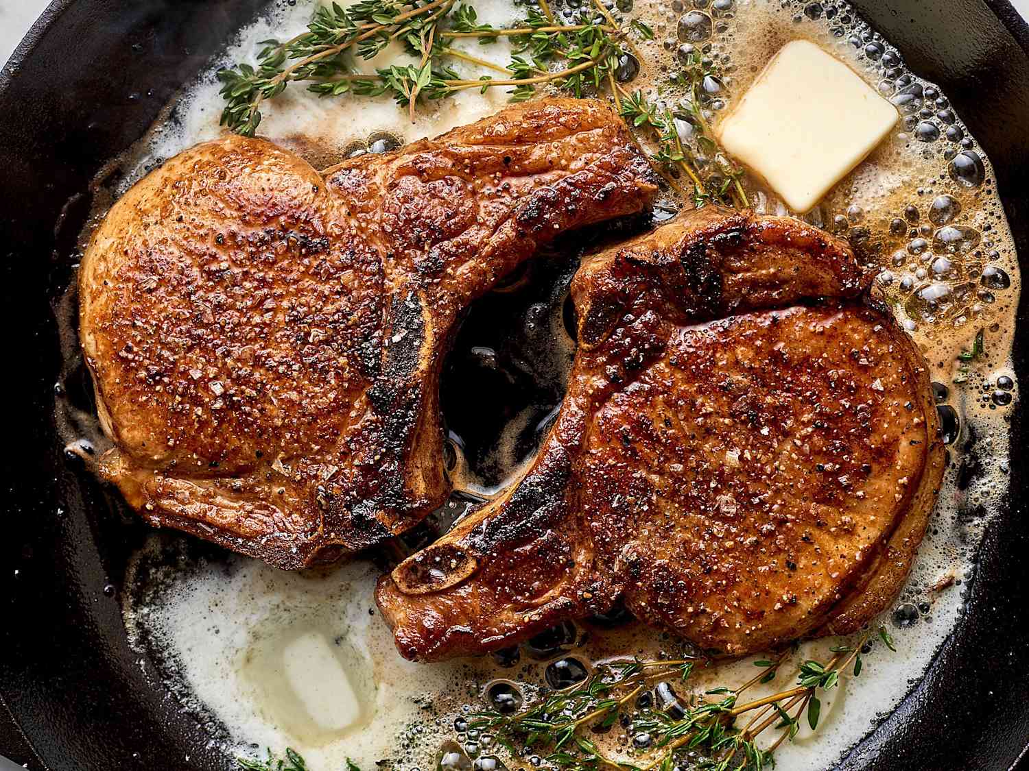 Pork chops searing in a cast iron skillet with browned crust forming along the edges on a stovetop