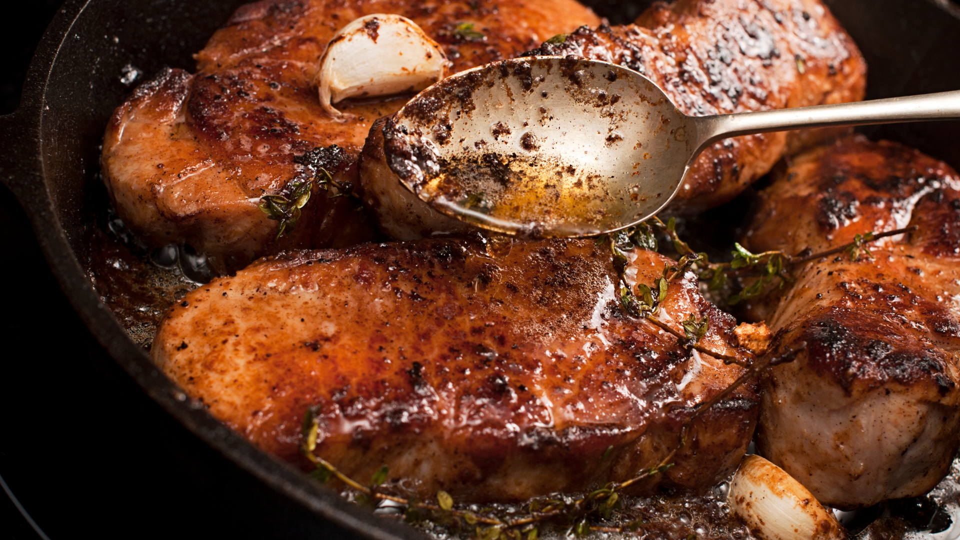 Pork loin chops browning in a black skillet with golden edges forming, seen from above on a home stove