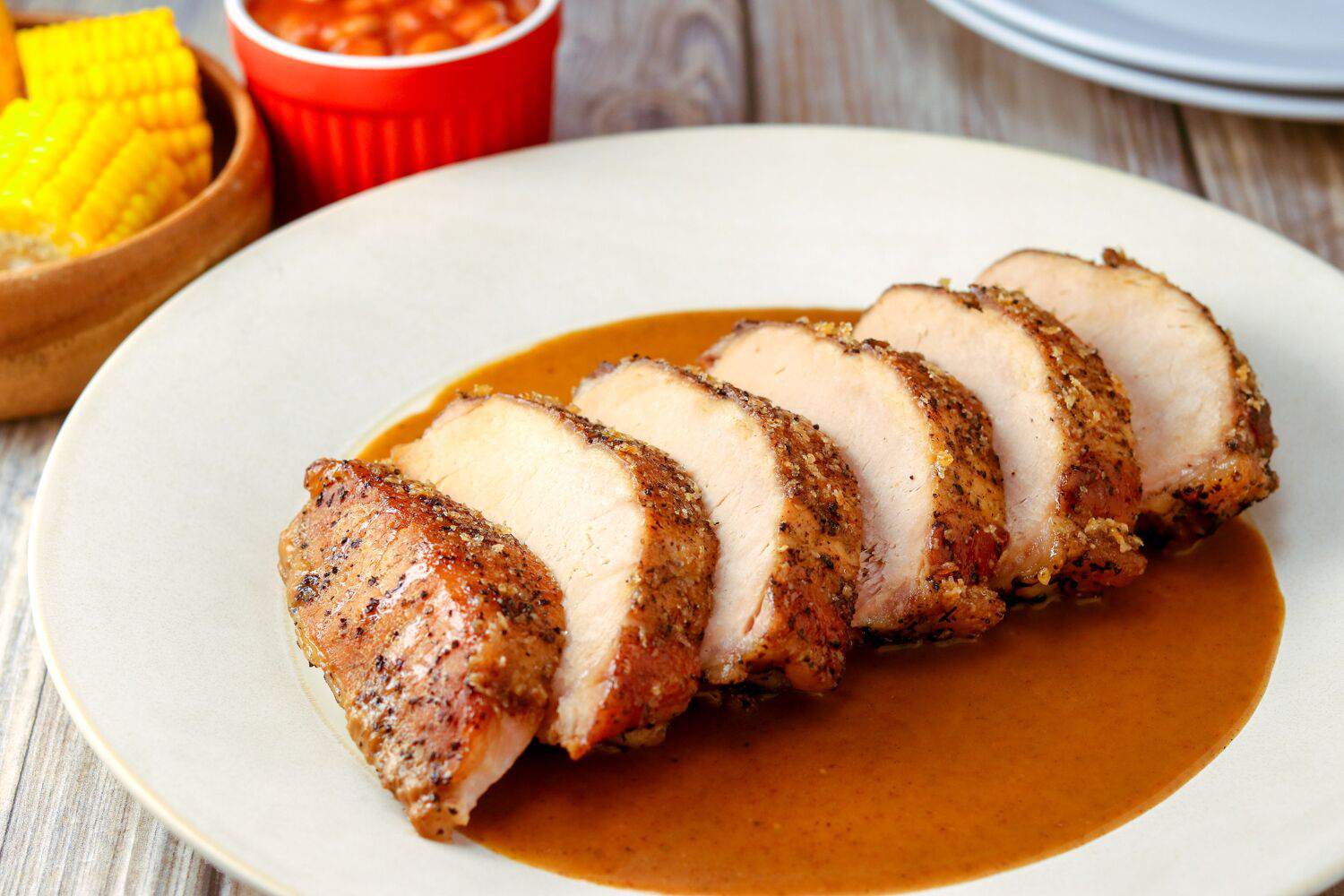 Pork loin nestled in a slow cooker with onions in broth, lid lifted to show steam