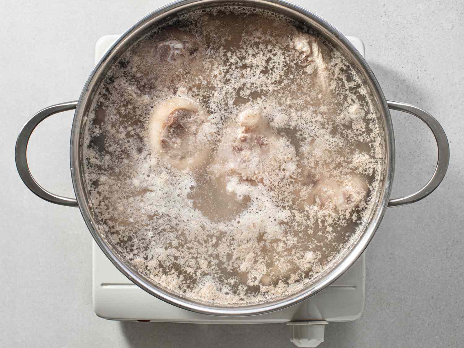 Pork neck bones and chicken backs arranged on a kitchen counter with garlic, ginger, scallions, and measuring cups ready for broth prep