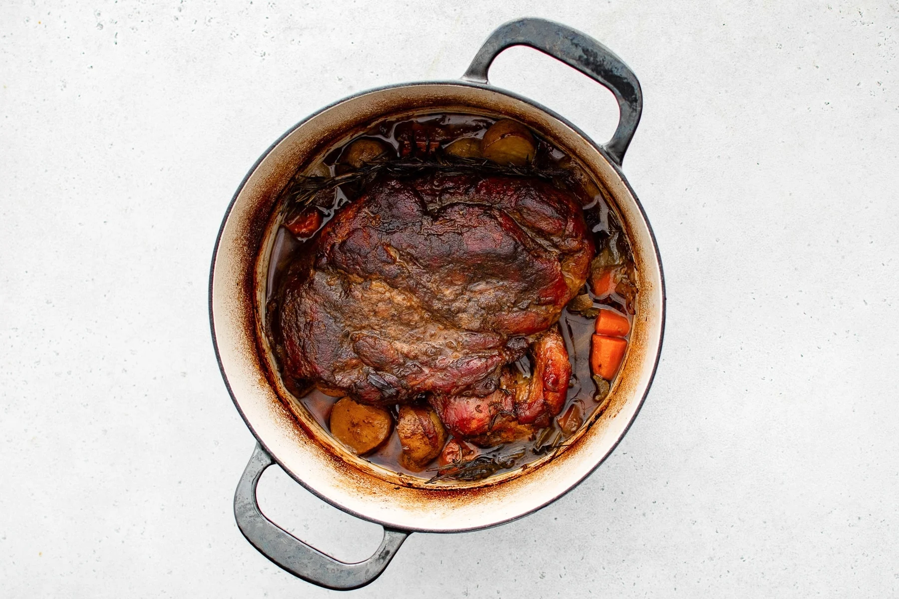 Pork pieces browning in a heavy pot on a stovetop with a wooden spoon nearby and steam rising