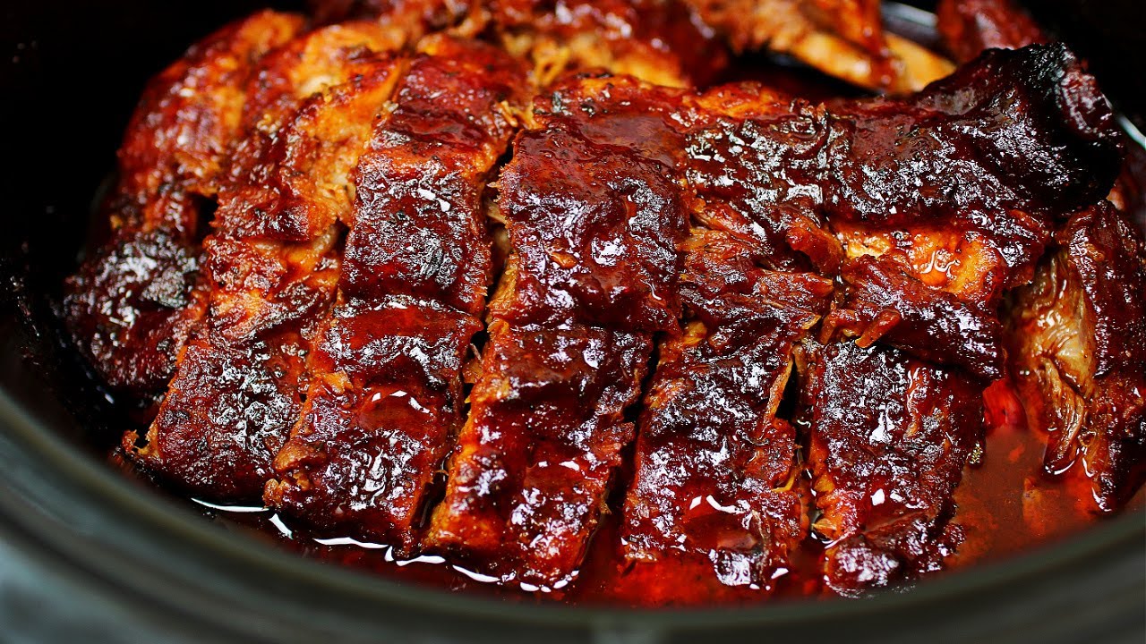 Pork ribs arranged upright in a slow cooker with sauce being poured over them