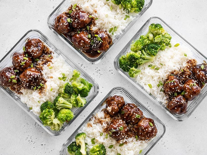 Portioned Swedish meatballs and gravy in glass meal prep containers on a kitchen counter with lids nearby