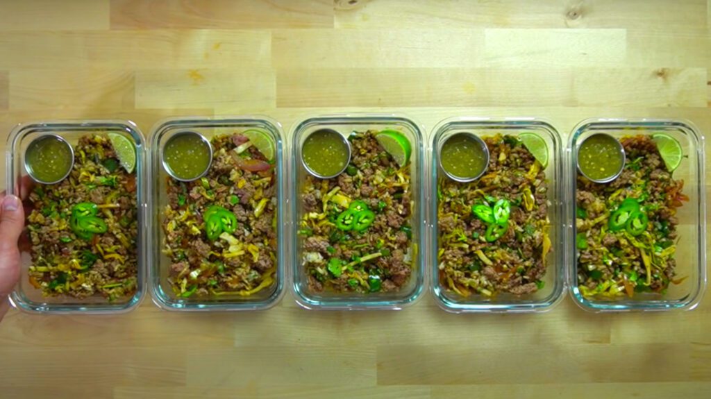 Portioned chile verde in clear glass meal prep containers with lids on a kitchen counter, ready for the refrigerator