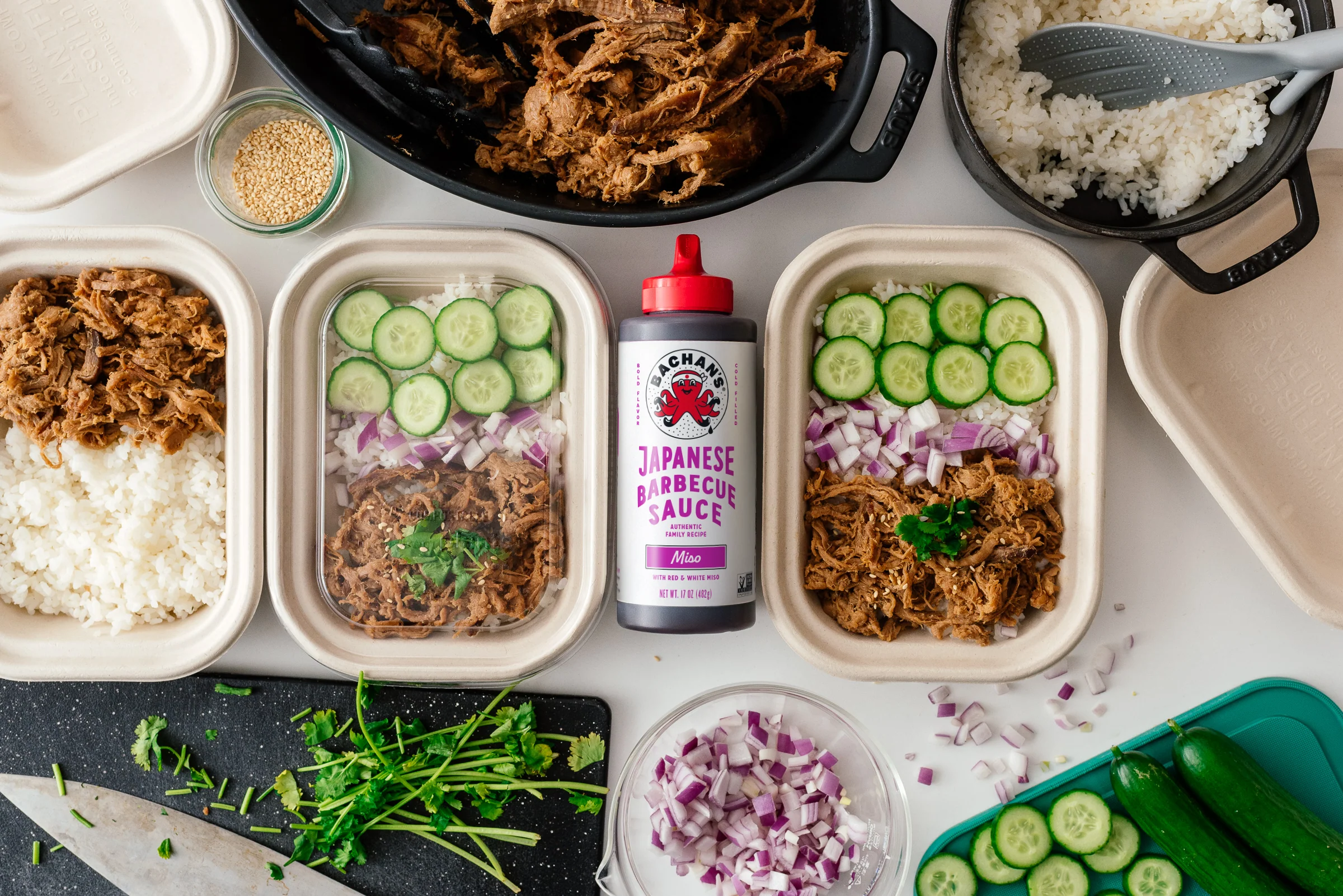Portioned pulled pork in glass meal prep containers with a little cooking juice at the bottom on a kitchen counter