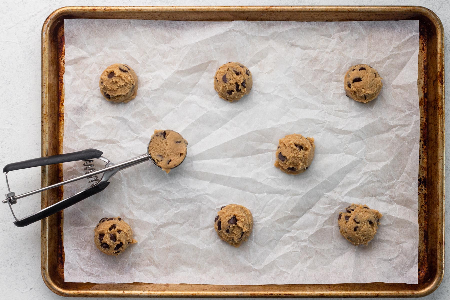 Portions of chocolate chip cookie dough arranged on a parchment-lined baking sheet before baking