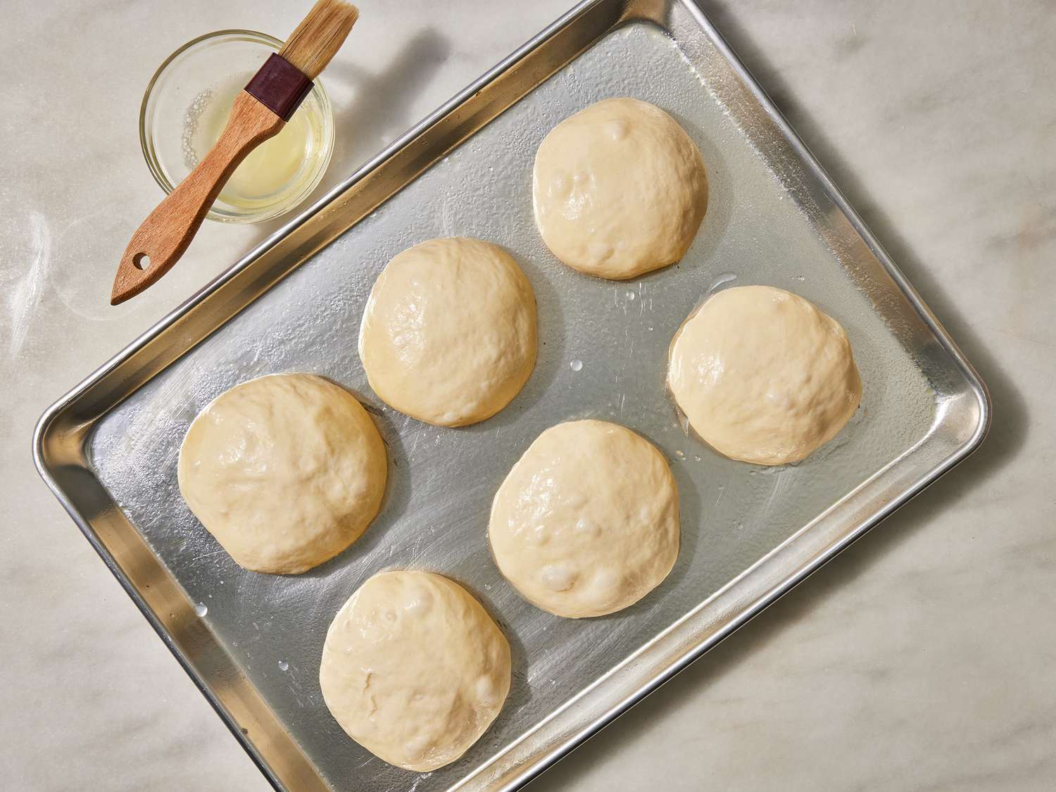 Portions of dough shaped into smooth round balls on a lightly floured countertop, with a parchment-lined baking sheet nearby