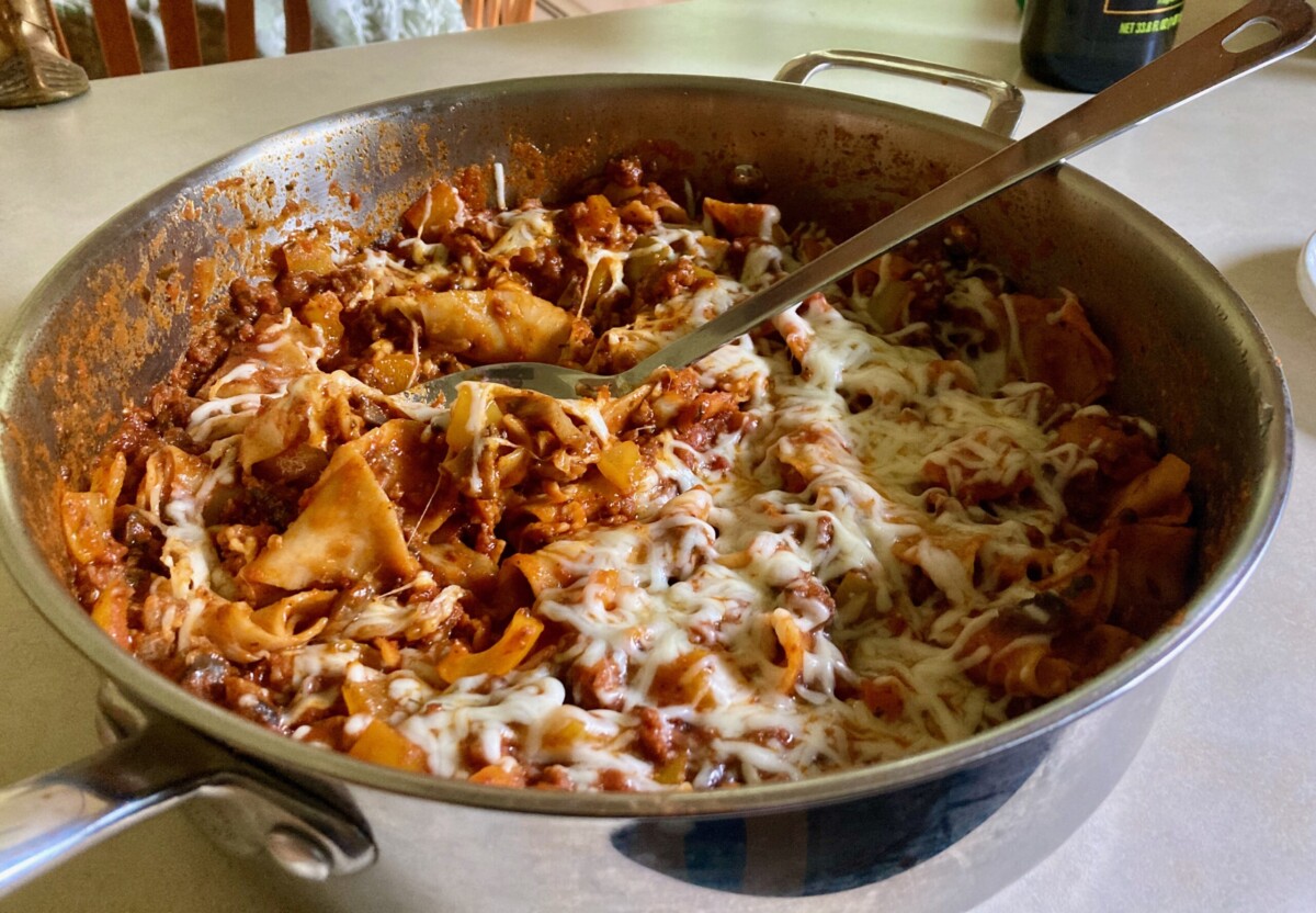 Portions of skillet lasagna stored in a clear airtight container on a kitchen counter, with a small container of extra basil nearby
