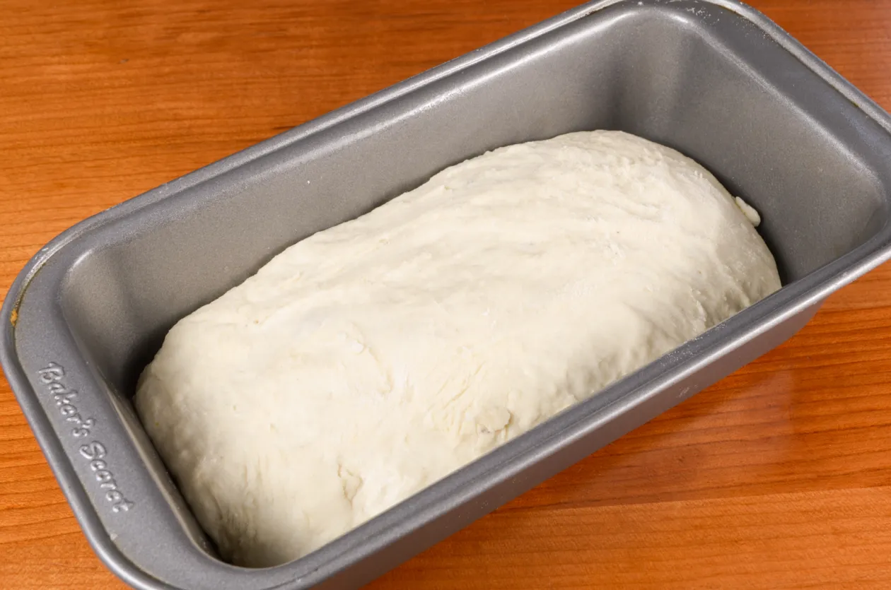 Potato bread dough shaped and placed in a greased loaf pan on a kitchen counter before rising