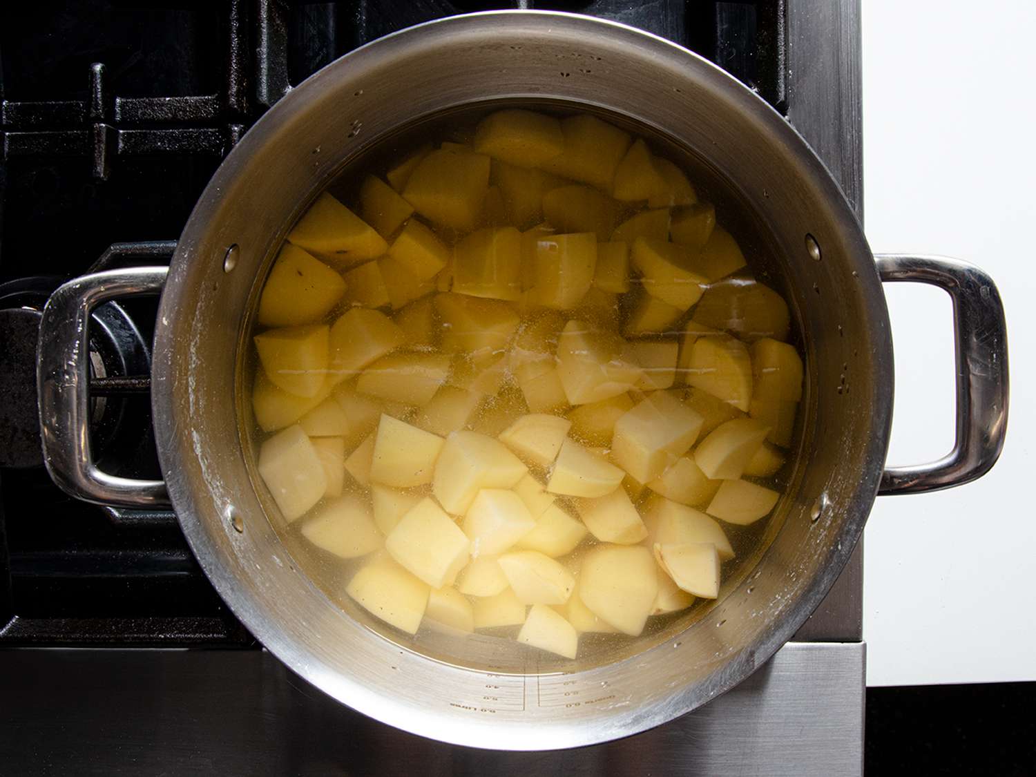 Potato chunks gently simmering in a large pot on a stovetop with light steam rising