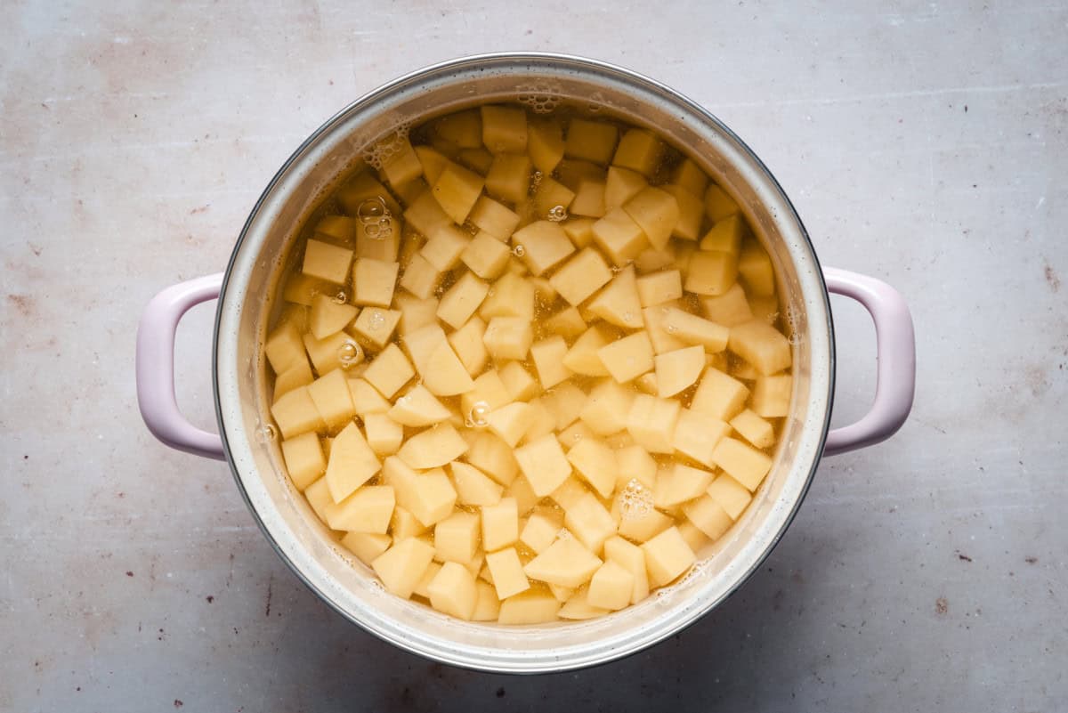 Potato chunks simmering in a saucepan of broth on a stovetop with gentle bubbles