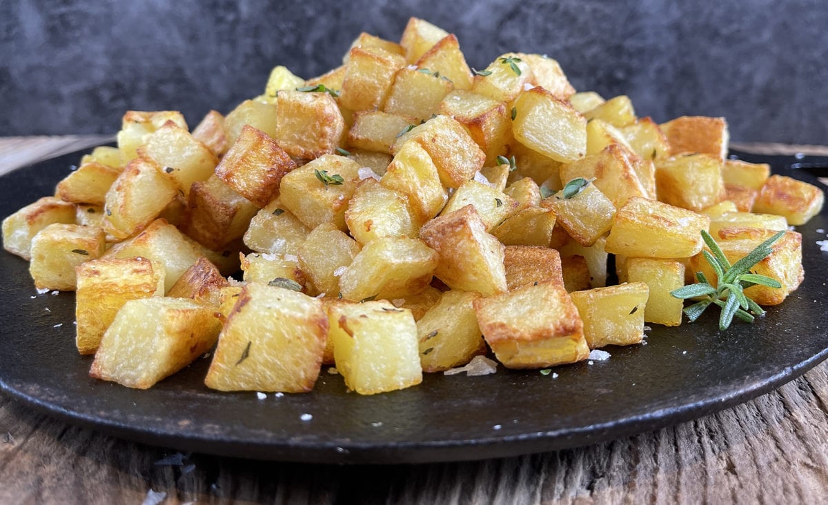 Potato cubes roasting on a metal sheet pan in a home oven, edges browned and crisp