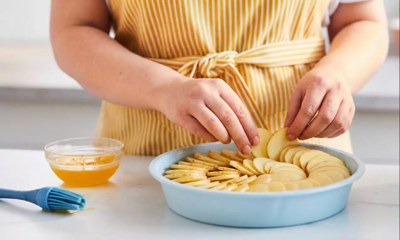 Potato slices overlapped in a neat spiral pattern inside a round pan, ready for buttering
