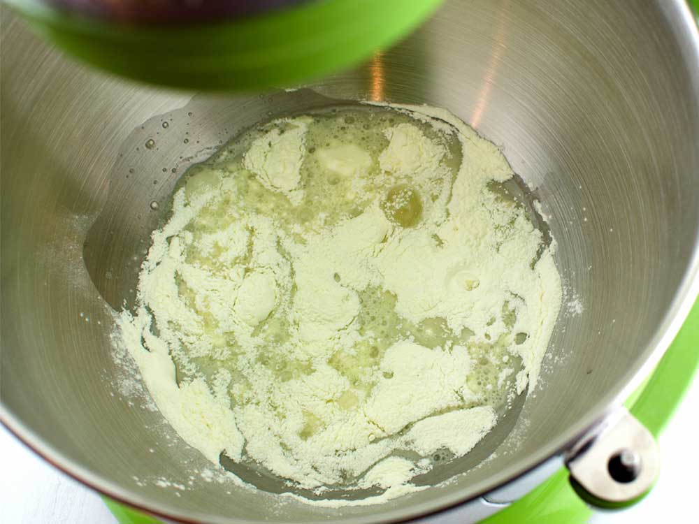 Powdered sugar, meringue powder, and a small bowl of water arranged on a tidy kitchen counter with measuring spoons