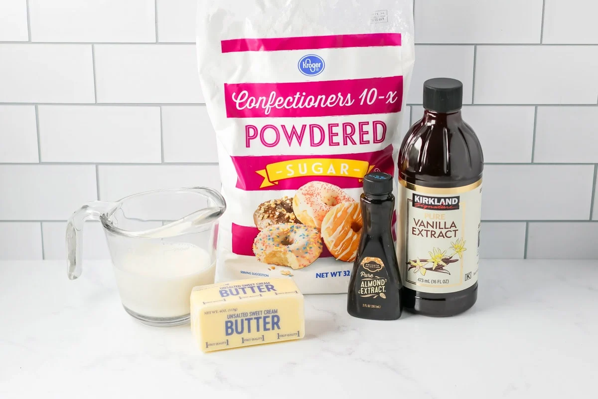Powdered sugar, softened butter, vanilla extract, milk, and a pinch of salt measured out on a clean kitchen counter