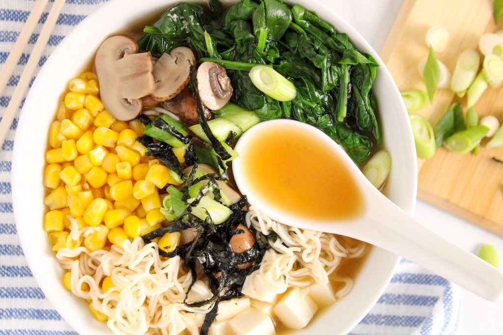 Prep bowls with sliced mushrooms, chopped scallions, torn nori, sesame seeds, and chili crisp arranged neatly on a kitchen counter in consistent warm lighting