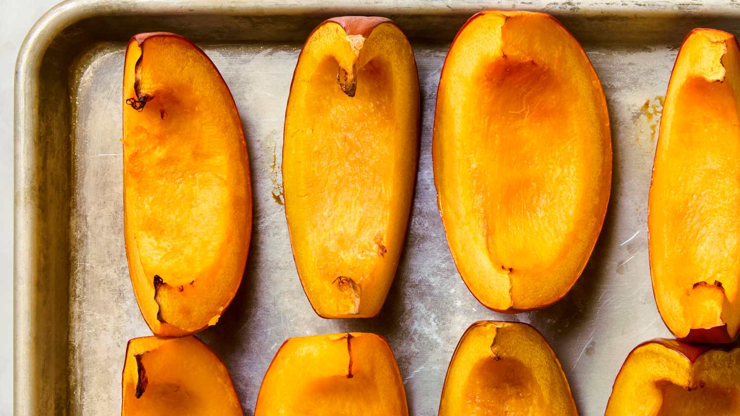 Pumpkin halves roasting cut side down on a rimmed baking sheet inside a home oven