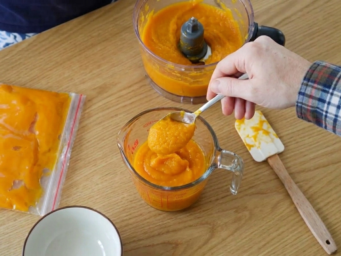 Pumpkin purée being spooned into a measuring cup with storage containers nearby