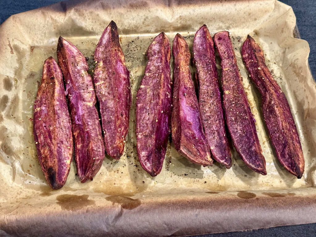 Purple sweet potato wedges in a bowl being tossed with olive oil and spices on a kitchen counter