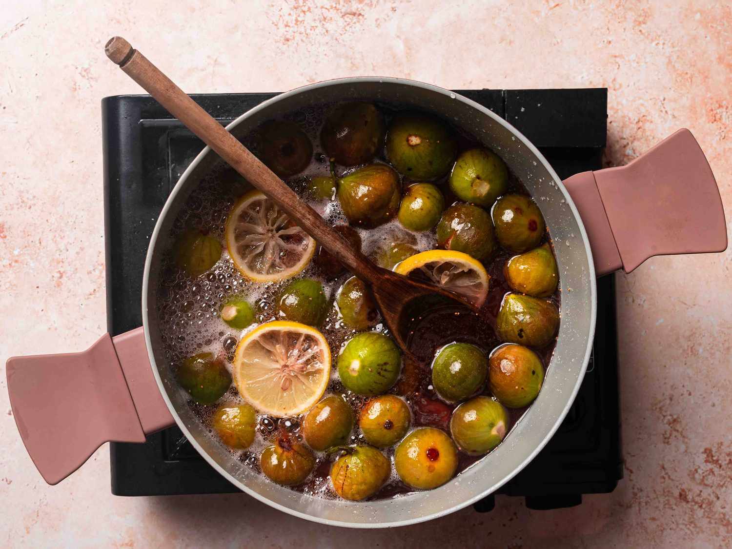 Quartered figs tossed with sugar and lemon in a saucepan, glistening as they release juices on a kitchen counter