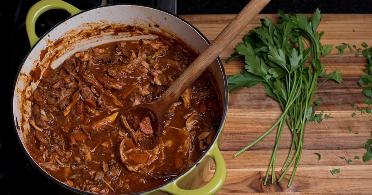 Rabbit ragu gently simmering in a Dutch oven on a stovetop with a wooden spoon resting nearby