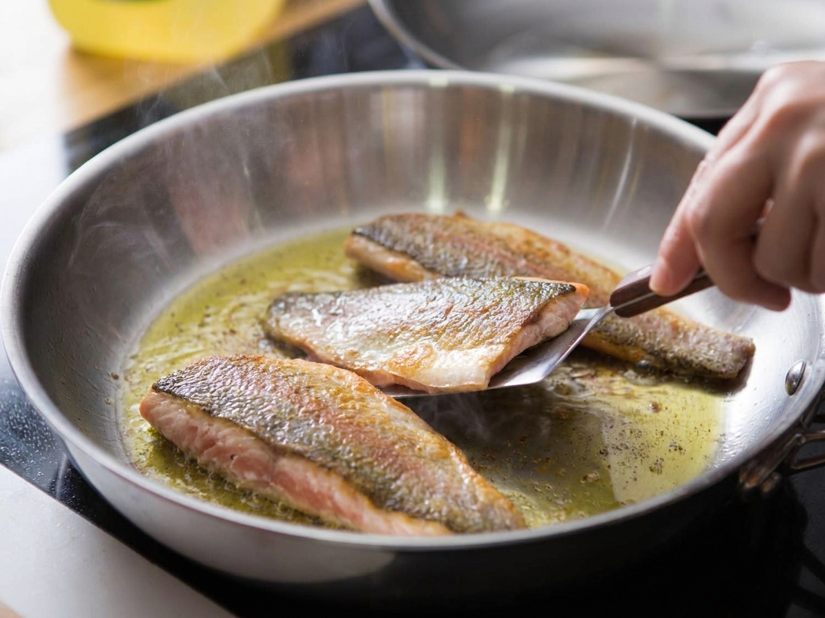 Rainbow trout fillets searing skin-side down in a skillet with edges turning opaque as the skin crisps