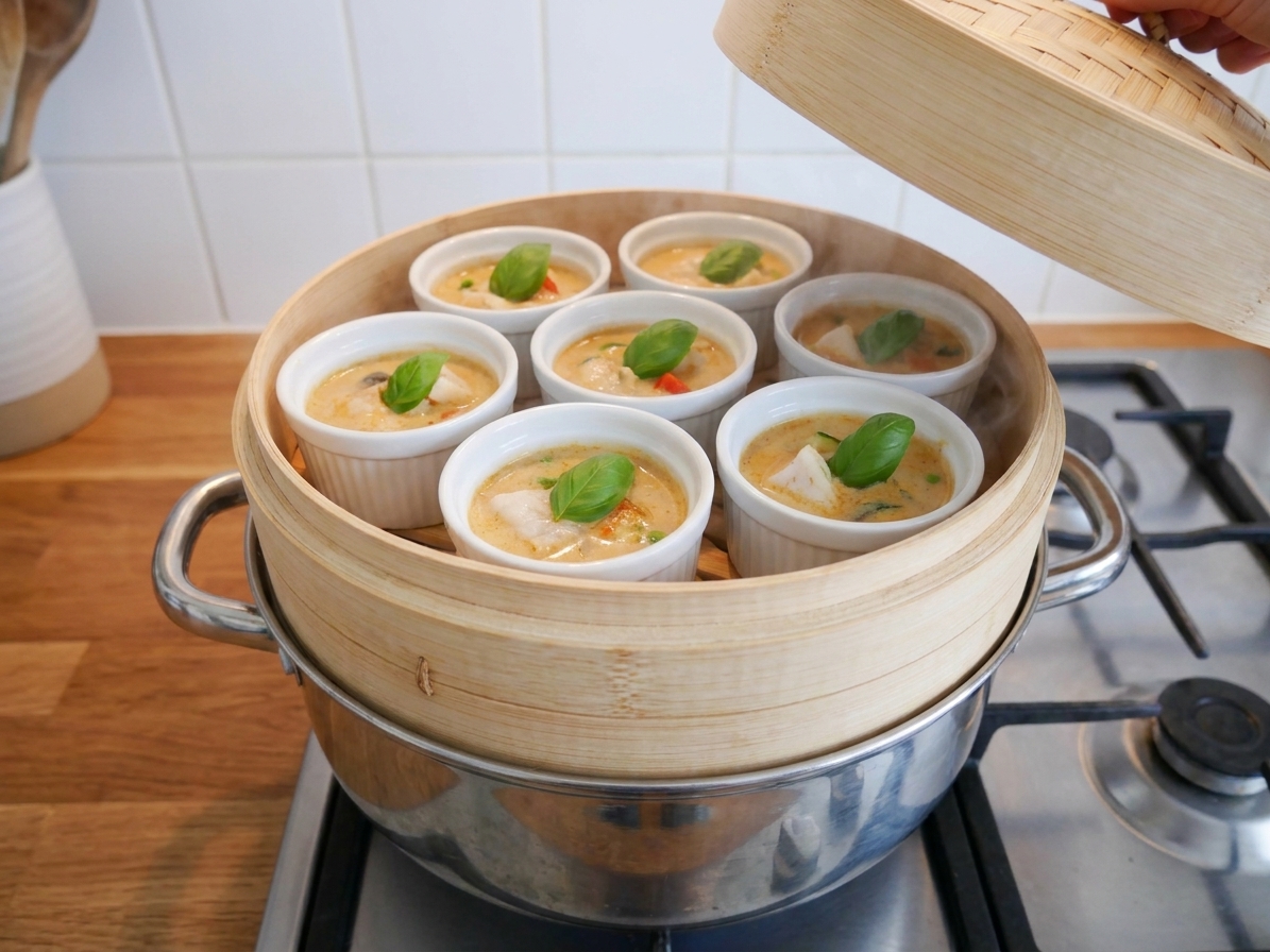 Ramekins filled with coconut fish curry sitting in a steamer basket over simmering water on a stovetop