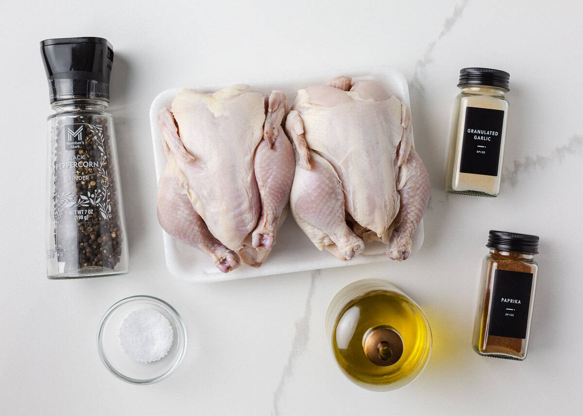 Raw Cornish hens, lemon, garlic, butter, olive oil, thyme, rosemary, salt, pepper, and chicken broth arranged on a light kitchen counter