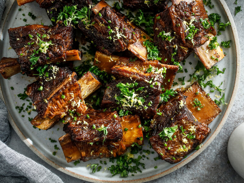Raw beef short ribs with carrots, celery, onion, tomato paste, garlic, red wine, beef stock, and fresh thyme arranged on a kitchen counter