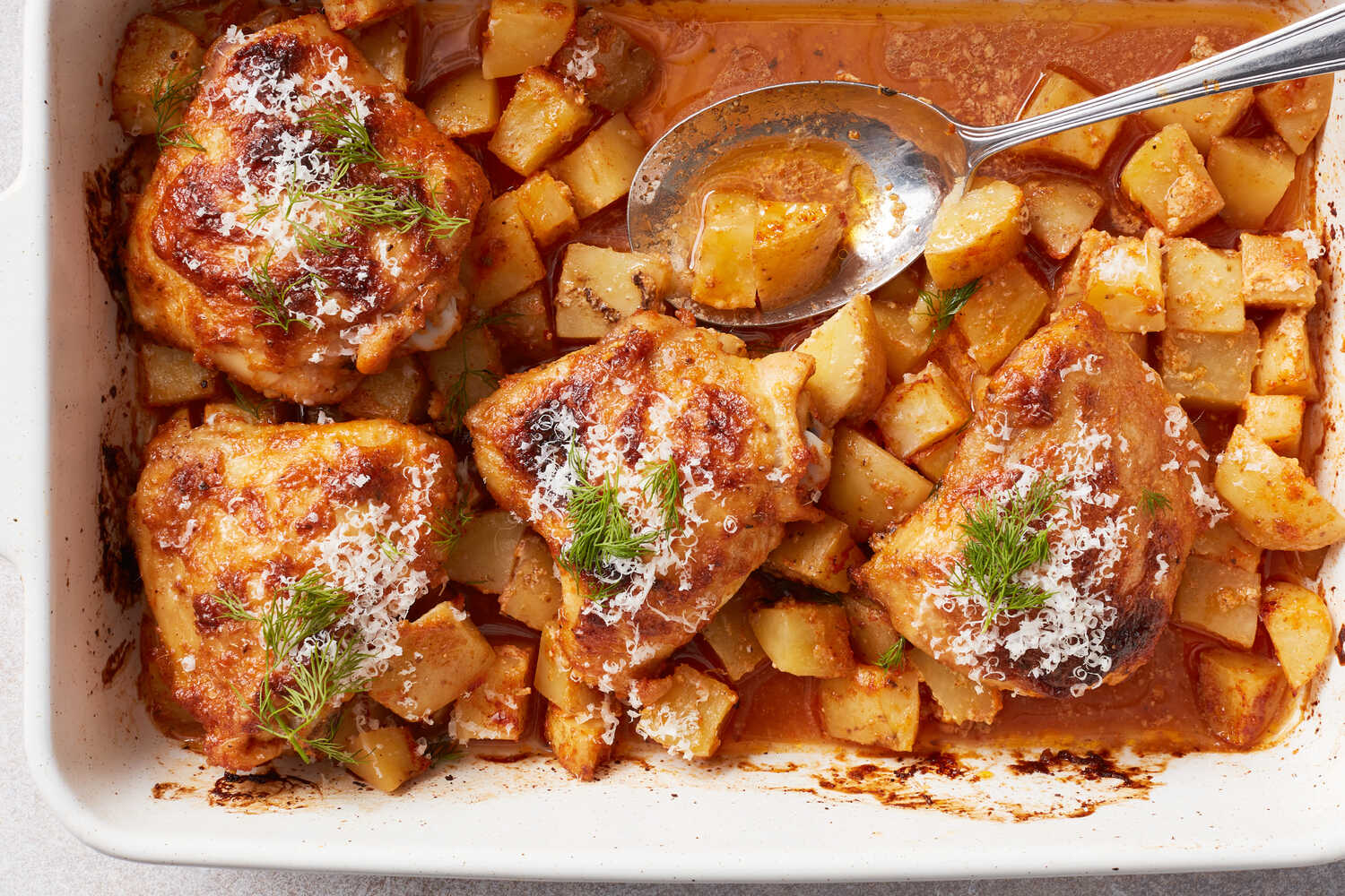 Raw bone-in chicken thighs, baby potatoes, garlic, lemon, olive oil, paprika, oregano, and salt arranged on a consistent light kitchen counter