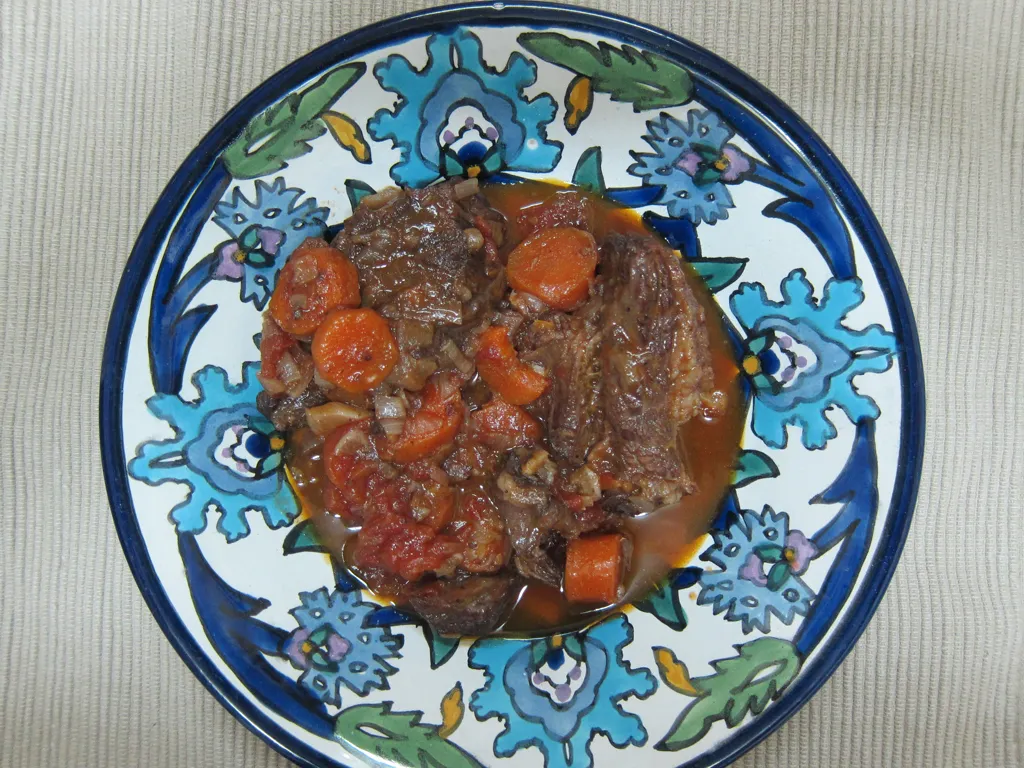 Raw camel meat cut into stew-sized chunks on a wooden cutting board with a chef's knife and a small bowl of salt nearby