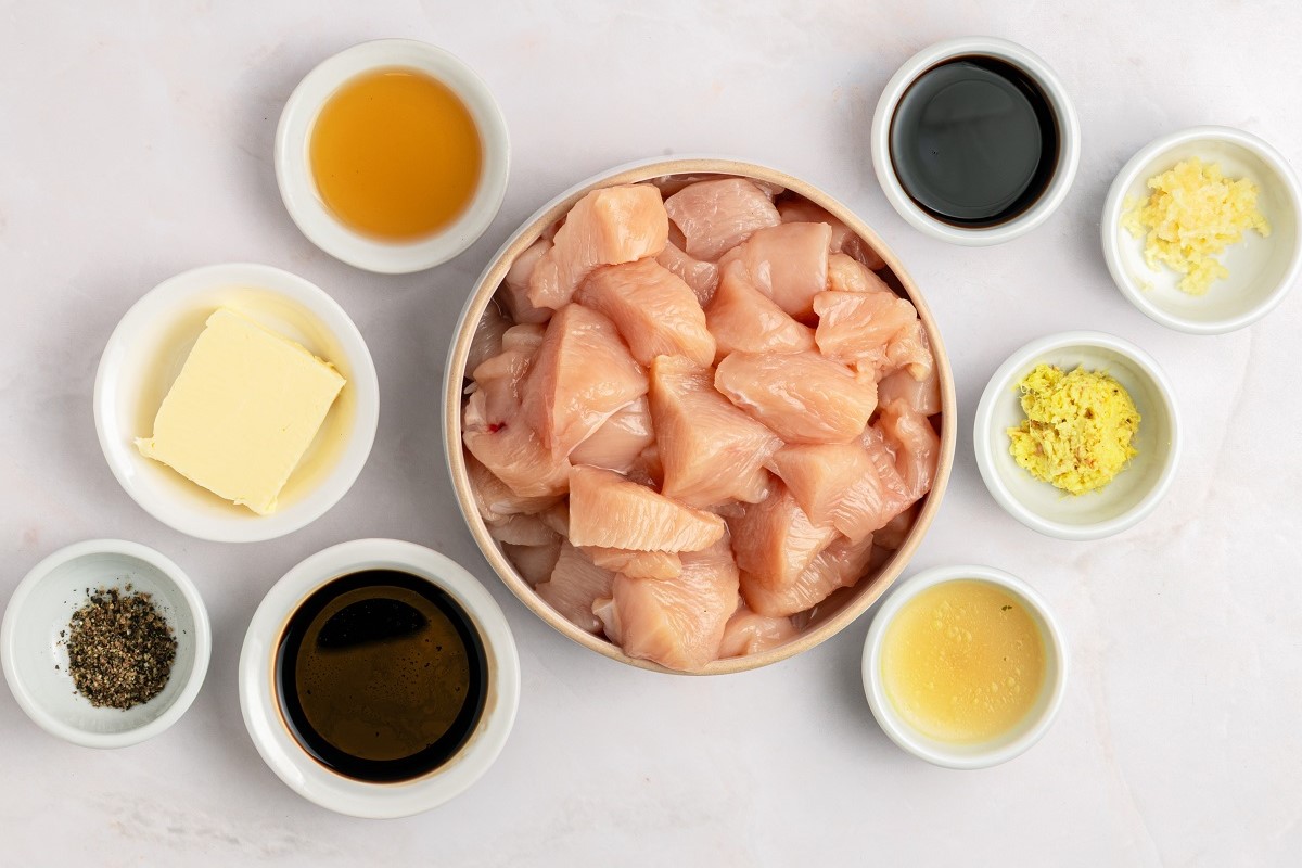 Raw chicken breast cubes, zucchini, onion, soy sauce, butter, garlic, ginger, sesame oil, and mayonnaise arranged on a clean kitchen counter with small prep bowls