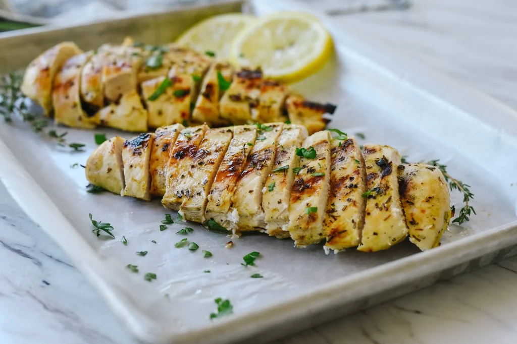 Raw chicken breasts coated in a lemony mustard marinade in a glass mixing bowl on a kitchen counter