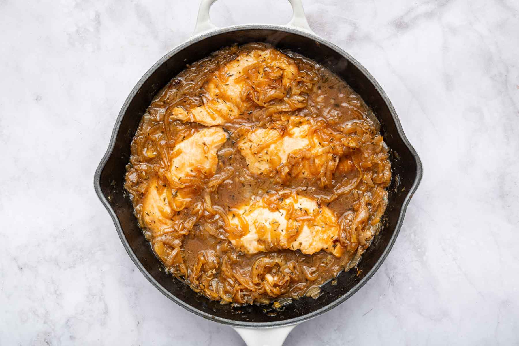 Raw chicken cutlets, onions, garlic, broth, milk, and seasonings arranged on a kitchen counter with a cutting board