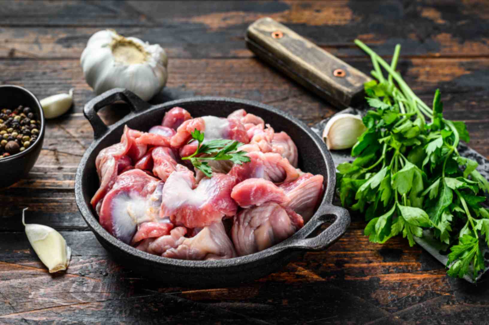 Raw chicken gizzards on a cutting board next to a bowl of buttermilk, flour, spices, and a lemon on a home kitchen counter