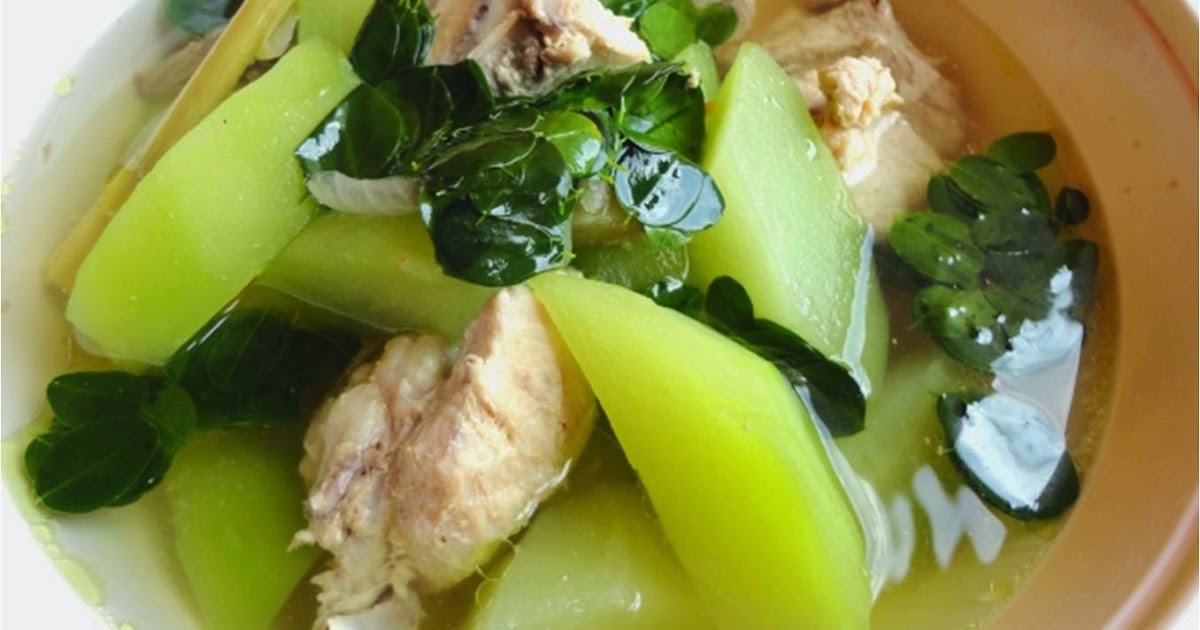 Raw chicken pieces, fresh ginger, garlic, onion, green papaya or chayote, fish sauce, and leafy greens arranged on a bright kitchen counter with a cutting board