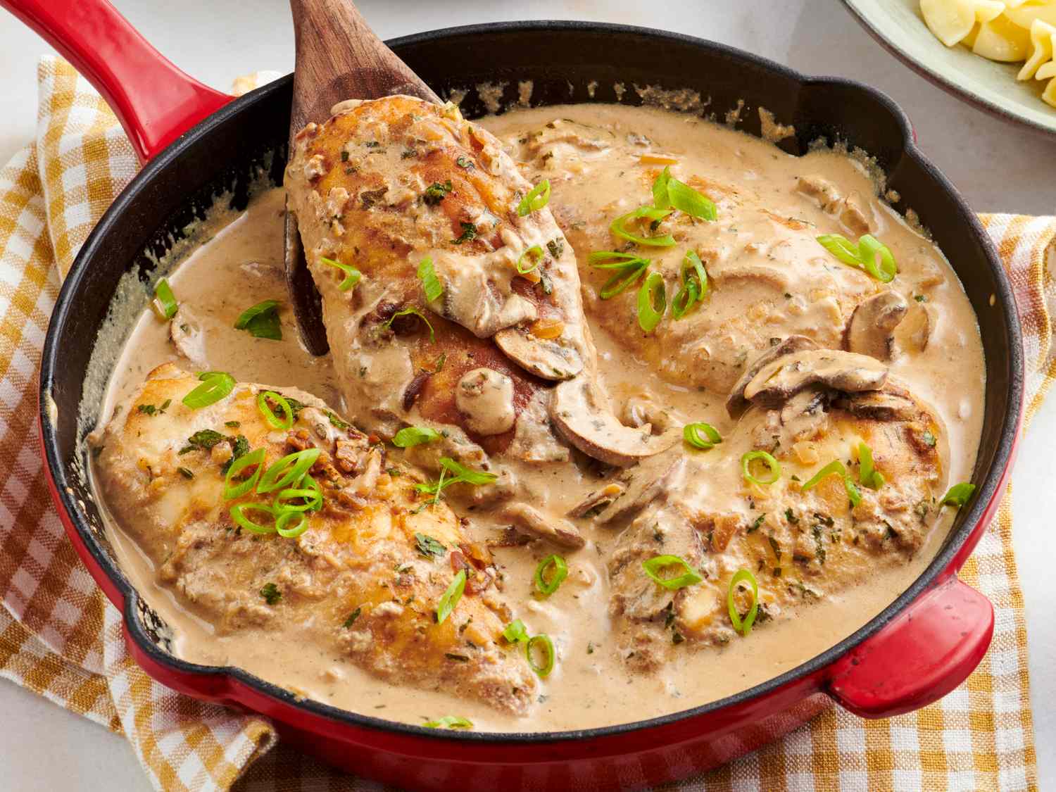 Raw chicken pieces, sliced mushrooms, sliced onion, garlic, sour cream, chicken broth, Dijon mustard, paprika, and egg noodles arranged together for cooking