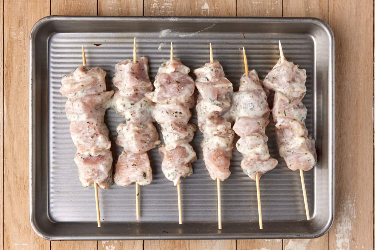 Raw chicken pieces threaded onto skewers on a parchment-lined sheet pan, ready for cooking