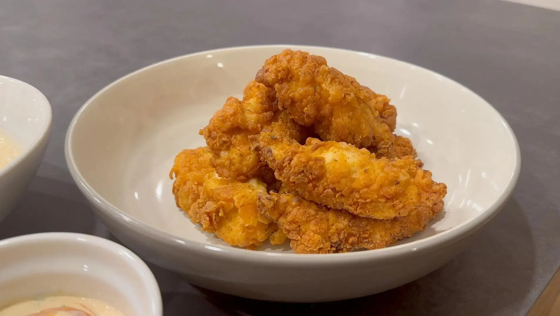 Raw chicken tenders soaking in a bowl of seasoned buttermilk on a bright kitchen counter with measuring spoons nearby