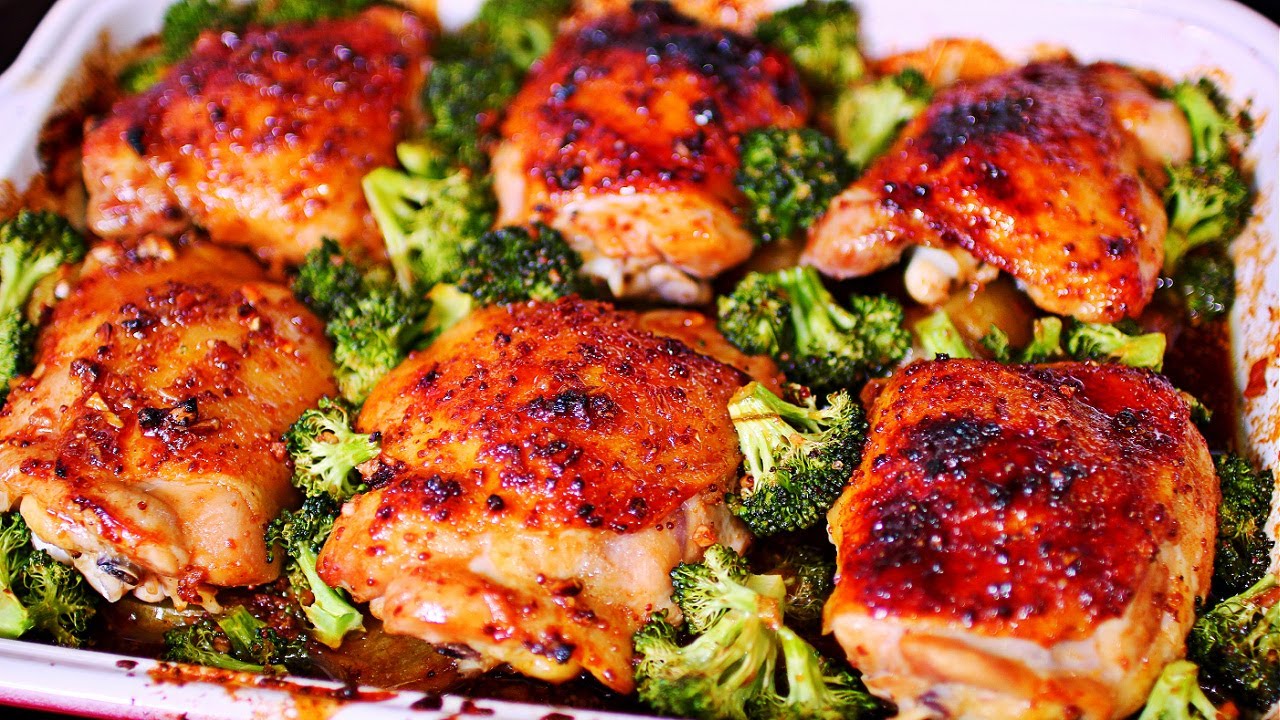 Raw chicken thighs, halved baby potatoes, broccoli florets, minced garlic, lemon, olive oil, and spices arranged in small bowls on a kitchen counter