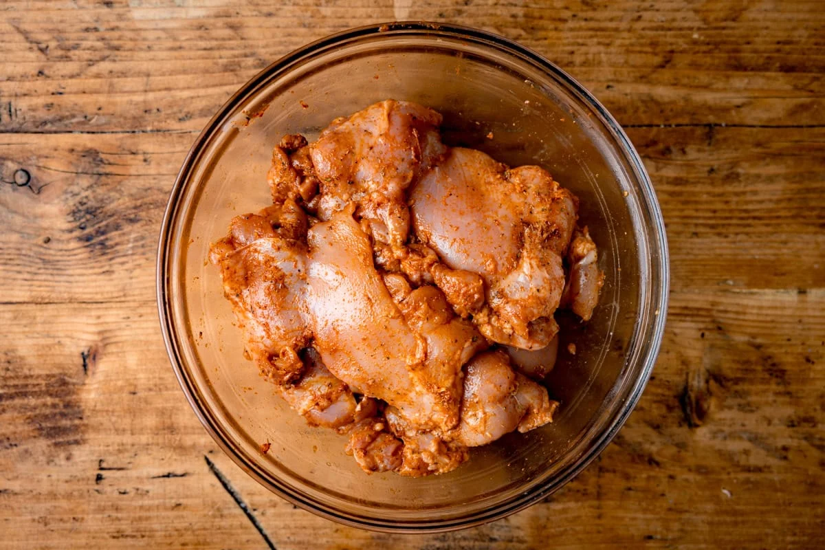 Raw chicken thighs in a bowl being mixed with yogurt, lemon, garlic, and spices for doner kebab marinade