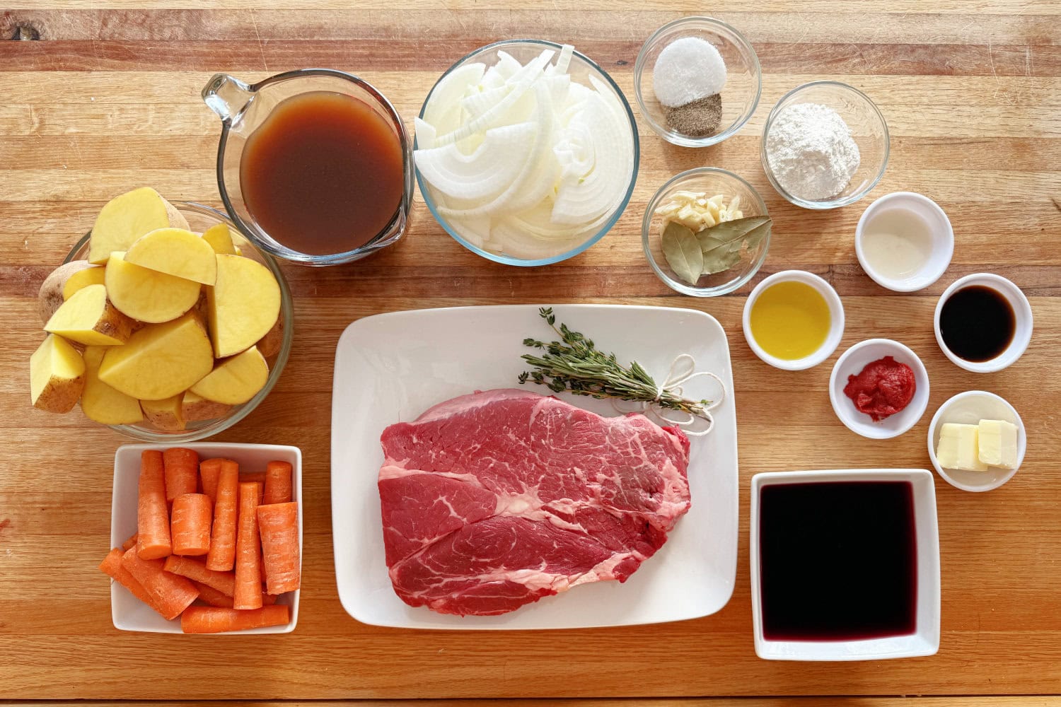 Raw chuck roast, potatoes, carrots, onion, garlic, beef broth, tomato paste, Worcestershire sauce, and seasonings arranged on a bright kitchen counter
